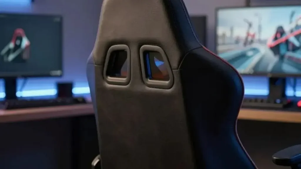 A close-up view of an ergonomic gaming chair, focusing on its durable materials, like high-quality synthetic leather and reinforced stitching. The chair, prominently positioned in the foreground, showcases its ergonomic design with adjustable features and a supportive backrest. In the middle ground, there's a blurred desktop with gaming paraphernalia, subtly indicating a gaming environment without being distracting. The background features a modern gaming setup, softly lit by ambient LED lights creating a cool and inviting atmosphere. The lighting emphasizes the textures of the chair's materials, highlighting their richness and sturdiness. This image exudes a sense of professionalism and durability, suitable for illustrating the importance of material quality in ergonomic gaming chairs. cadeira gamer barata e resistente